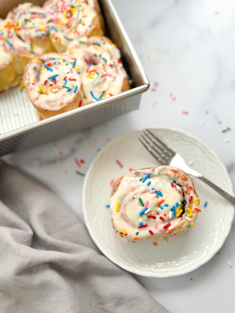 A pan of gluten-free cinnamon rolls topped with frosting and colorful sprinkles, showcasing a delicious dessert option.