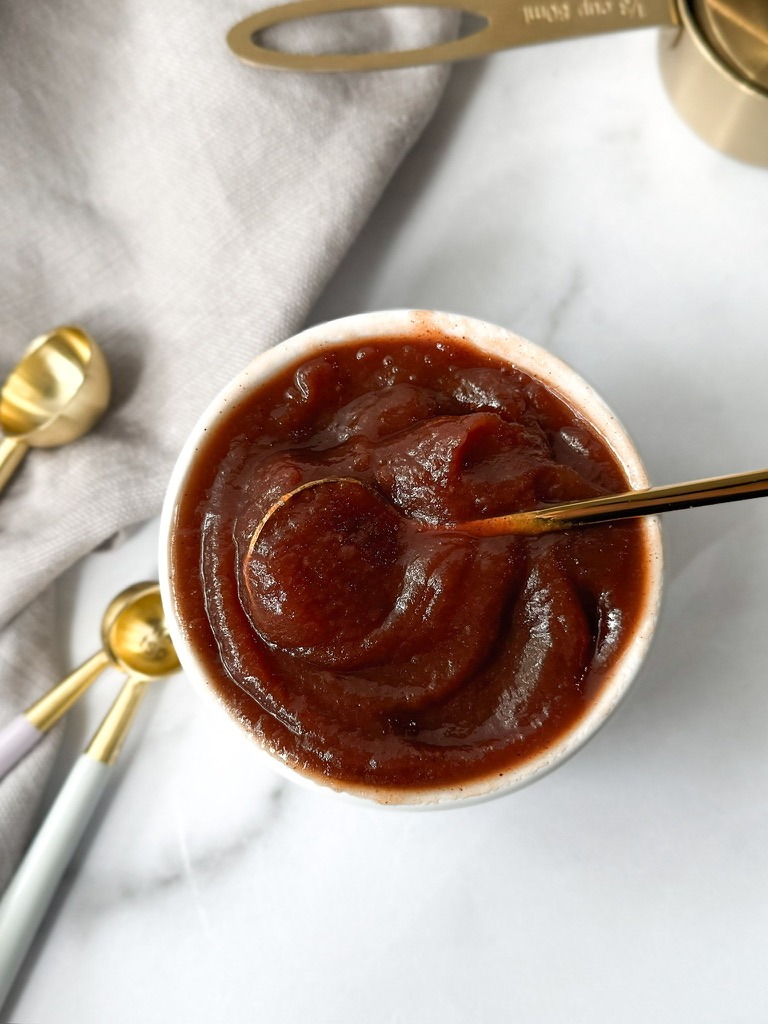 A clear jar filled with homemade apple butter, highlighting its vibrant hue, surrounded by fresh apples and spices.