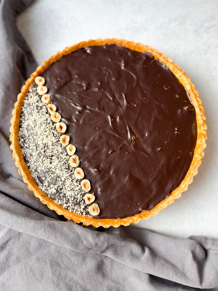 A rich chocolate tart featuring caramel and hazelnuts, beautifully topped with chocolate and a mix of crunchy nuts.
