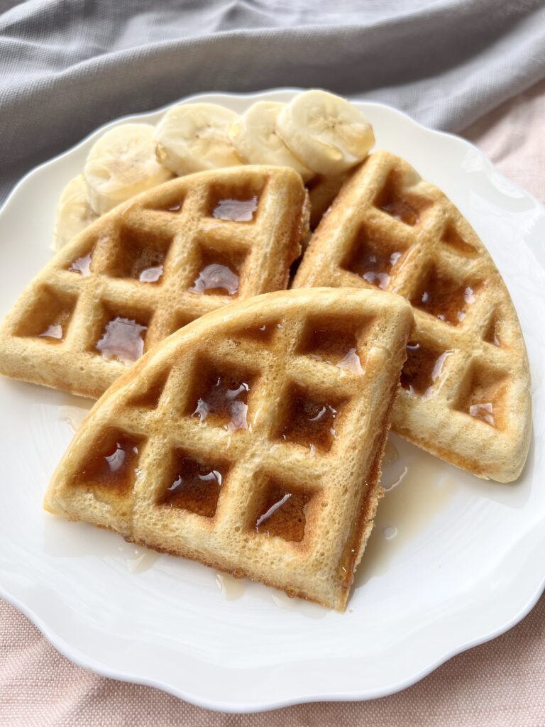 white plate with waffles drizzled with maple syrup